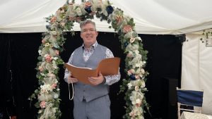 Wedding celebrant standing under floral arch during outdoor ceremony