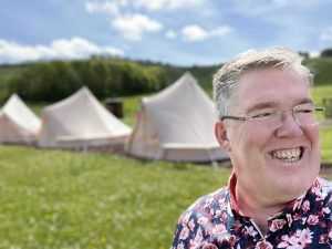 Smiling man outdoors with countryside lodges in the background